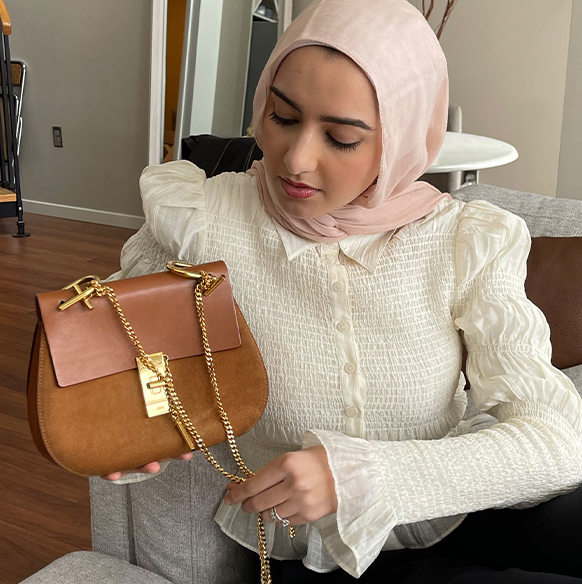 Fashion Blogger Summer Albarcha wears a scarf and long sleeved shirt, holding up a brown Chloé bag