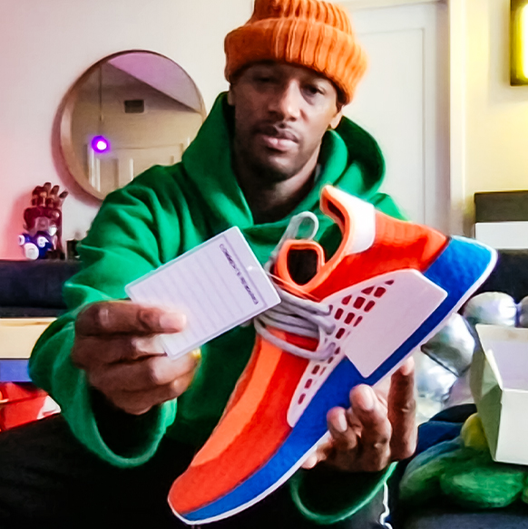 Designer Mateo Berry wears a hoodie and beanie holding up a sneaker with tags